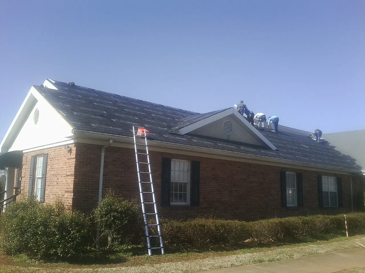 Crew tearing shingles off a brick ranch roof with a ladder set — Metal Roof Repair work by our crew in Sprague