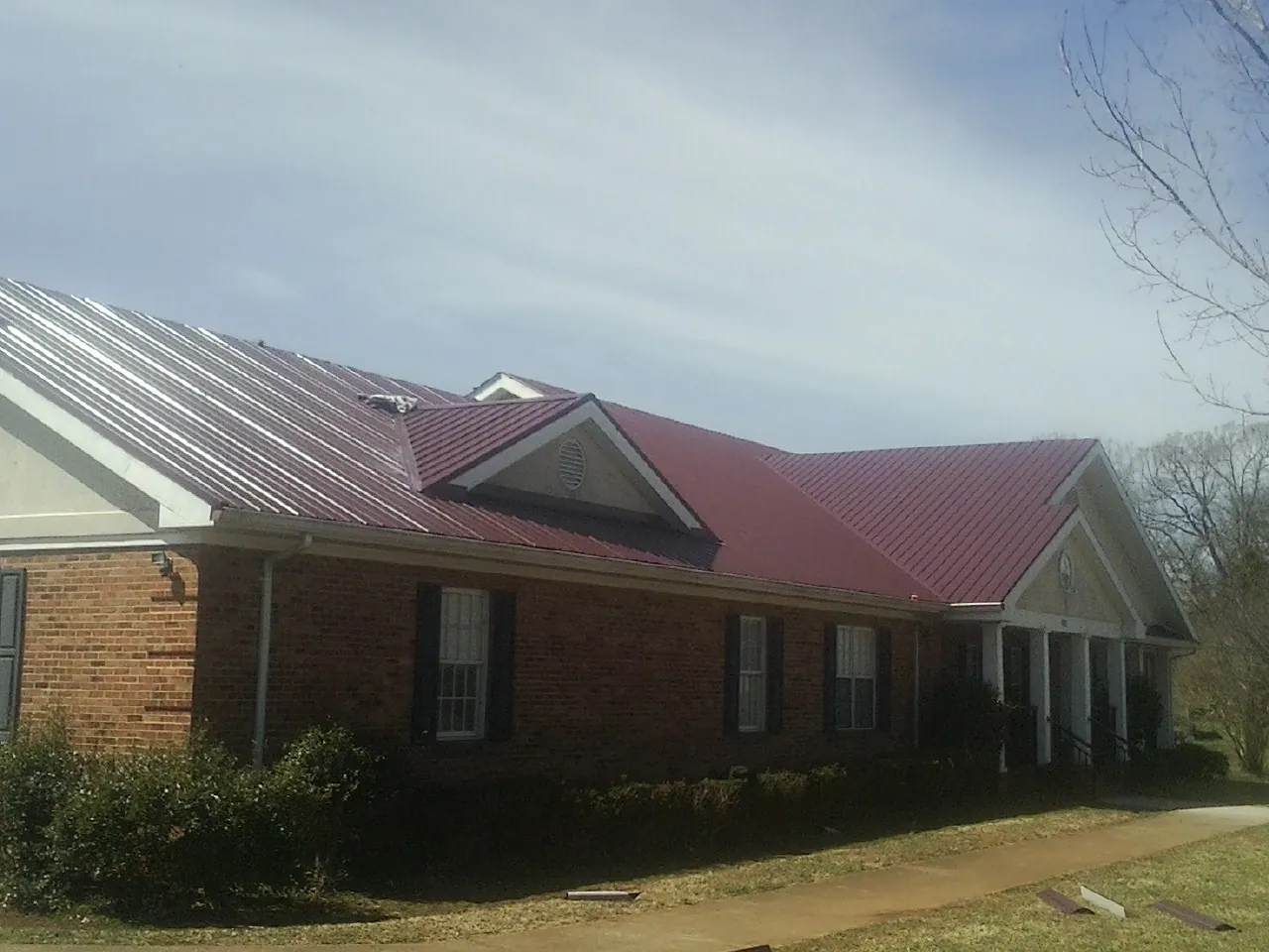 Red metal roof with gabled entries on a long brick building, from a Hail Damage Roof Repair job in Sprague