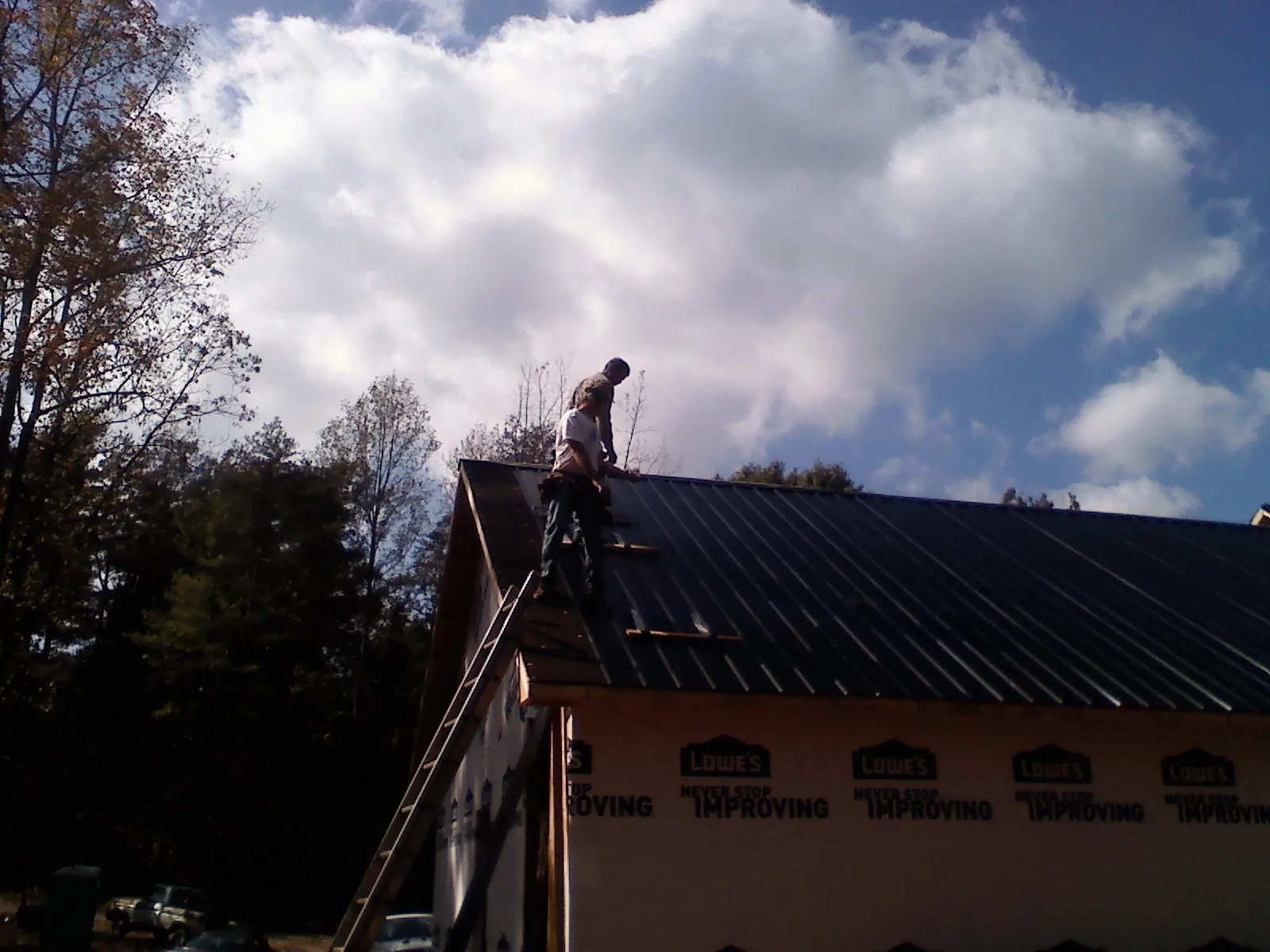 Roofer fastening dark metal panels high against a cloudy sky, from a Roof Inspection job in Sprague