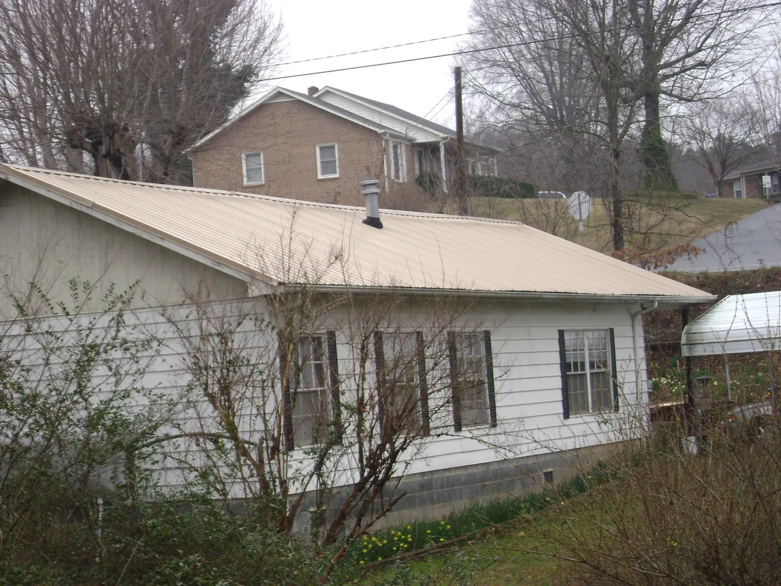 Tan metal roof on a white sided house set into a hillside — Commercial Roofing by Roofing Brothers in Sprague